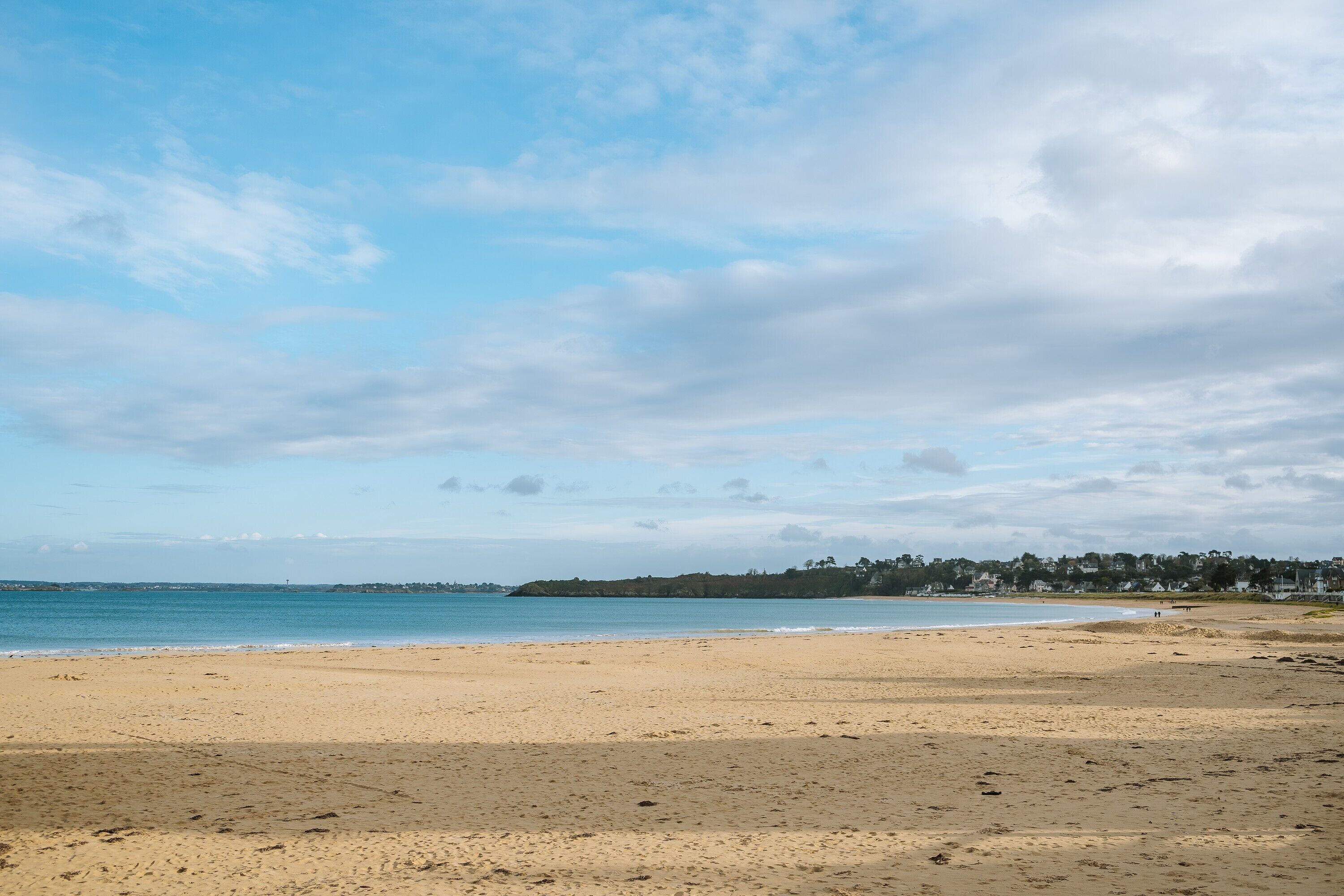 Une plage avec un ciel dégagé, une mer calme et une côte lointaine.
