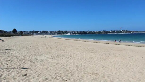 A wide sandy beach with clear blue water and a distant shoreline.