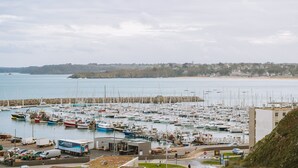 A marina with numerous boats docked, a building with a sign reading 'POR DE SAINTES,' and a view of the coastline.