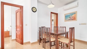A dining area with a wooden table and chairs, a clock on the wall, and a painting above the table. - Apartment 'Las Palmeras A92' with Sea Views, Shared Pool and Wi-Fi (MÁLAGA)