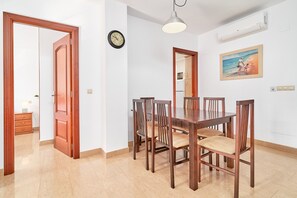A dining area with a wooden table and chairs, a clock on the wall, and a painting above the table.