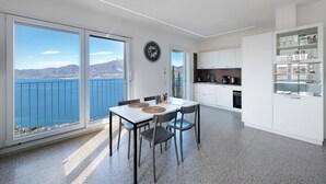A modern kitchen with white cabinets, a dining area with a table and chairs, and large windows with a view of the sea and mountains. - Apartment 'Casa Serena' with Lake View, Wi-Fi and Air Conditioning (Torri del Benaco)