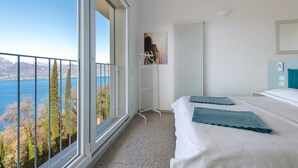 A bedroom with a large window, a bed, a bedside table, and a view of the sea. - Apartment 'Casa Serena' with Lake View, Wi-Fi and Air Conditioning (Torri del Benaco)