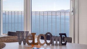 A view of the ocean through large windows with a balcony railing, a table with a woven placemat, and wooden letters spelling 'WELCOME'. - Apartment 'Casa Serena' with Lake View, Wi-Fi and Air Conditioning (Torri del Benaco)