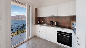 A modern kitchen with a view of the sea, a dining area with outdoor seating, and a built-in oven. - Apartment 'Casa Serena' with Lake View, Wi-Fi and Air Conditioning (Torri del Benaco)
