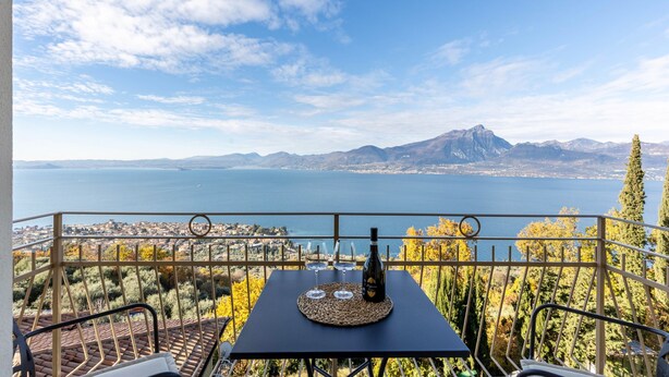 A terrace with a table, two wine glasses, and a bottle, overlooking a lake and mountains. - Apartment 'Casa Serena' with Lake View, Wi-Fi and Air Conditioning (Torri del Benaco)
