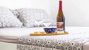 Una cama con almohadas estampadas, una botella de vino, dos copas y un cuenco decorativo sobre una bandeja.