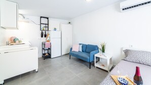 Un espacio habitable compacto con kitchenette, un sofá, una mesa pequeña y una cama.