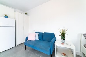 Un espacio habitable moderno y minimalista con un sofá azul, armarios blancos y una pequeña mesa con un florero.
