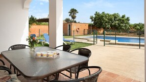 Un patio con mesa, sillas y vistas a una piscina y follaje.