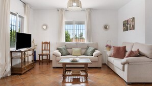 Una sala de estar con sofá, mesa de centro, televisor y ventana con cortinas.