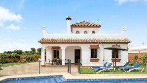 Una villa blanca con piscina, un patio amurallado y una sombrilla de paja.