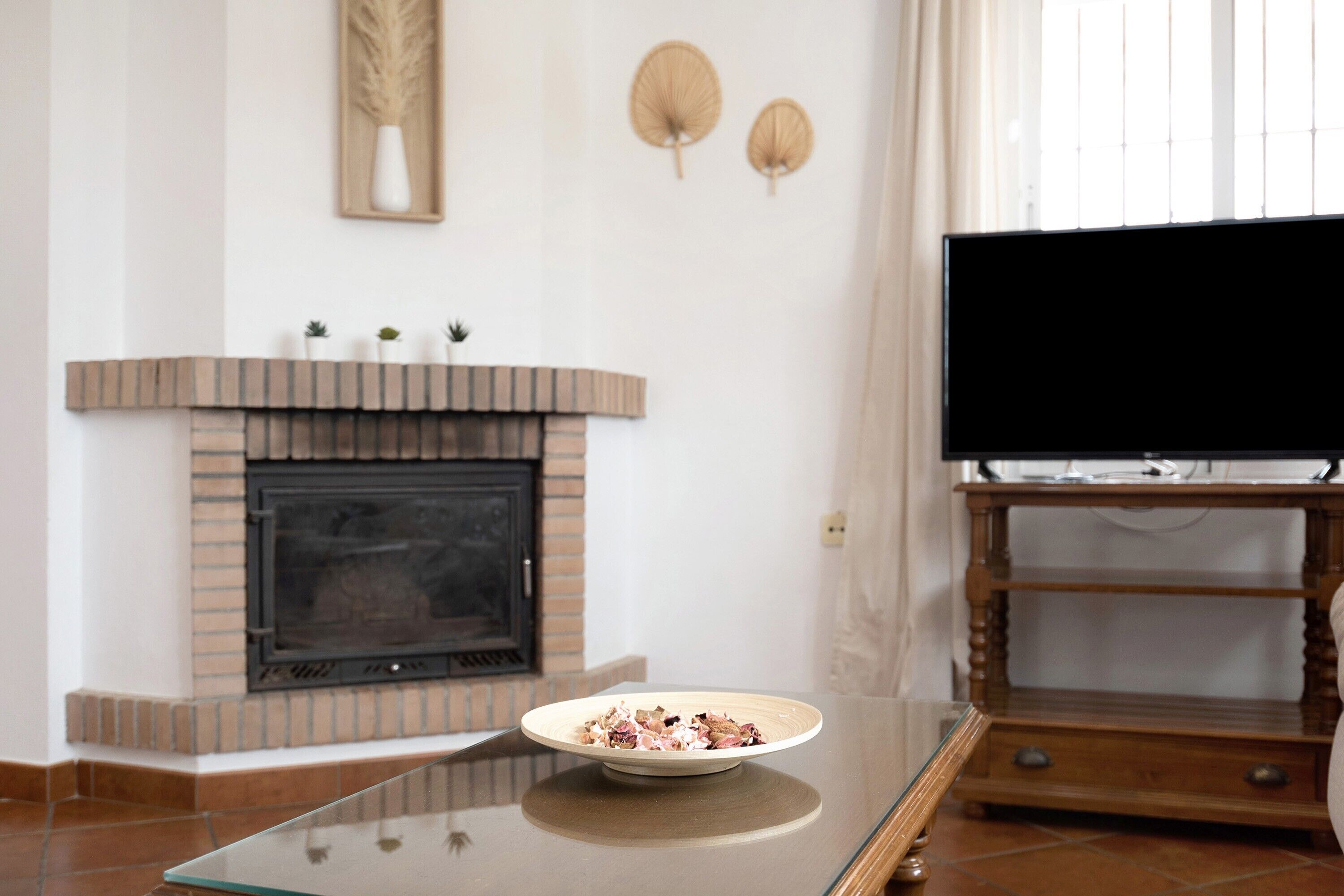 A living room with a fireplace, a television on a wooden stand, and a glass table with a bowl.