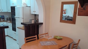 A dining area with a round wooden table and four chairs, a kitchen in the background, and a mirror on the wall.