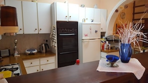A kitchen with white cabinets, a black oven, and a white refrigerator. There is a vase with dried plants on the counter.