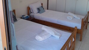 A room with two wooden beds, each with a white mattress and a pillow. There are towels on the beds, and a wardrobe with a light-colored door is visible in the background.