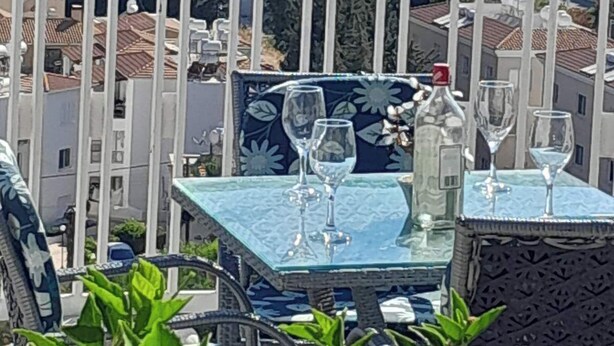 A terrace with a table set for two, overlooking a coastal cityscape.
