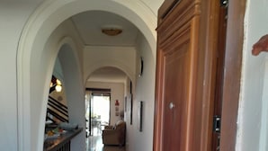 A hallway with a wooden door, white walls, and an arched doorway leading to a dining area.