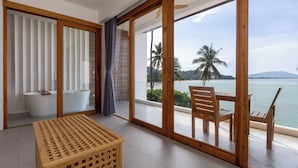 Una habitación moderna con un amplio ventanal corredera que da a un balcón con vistas al mar y palmeras.