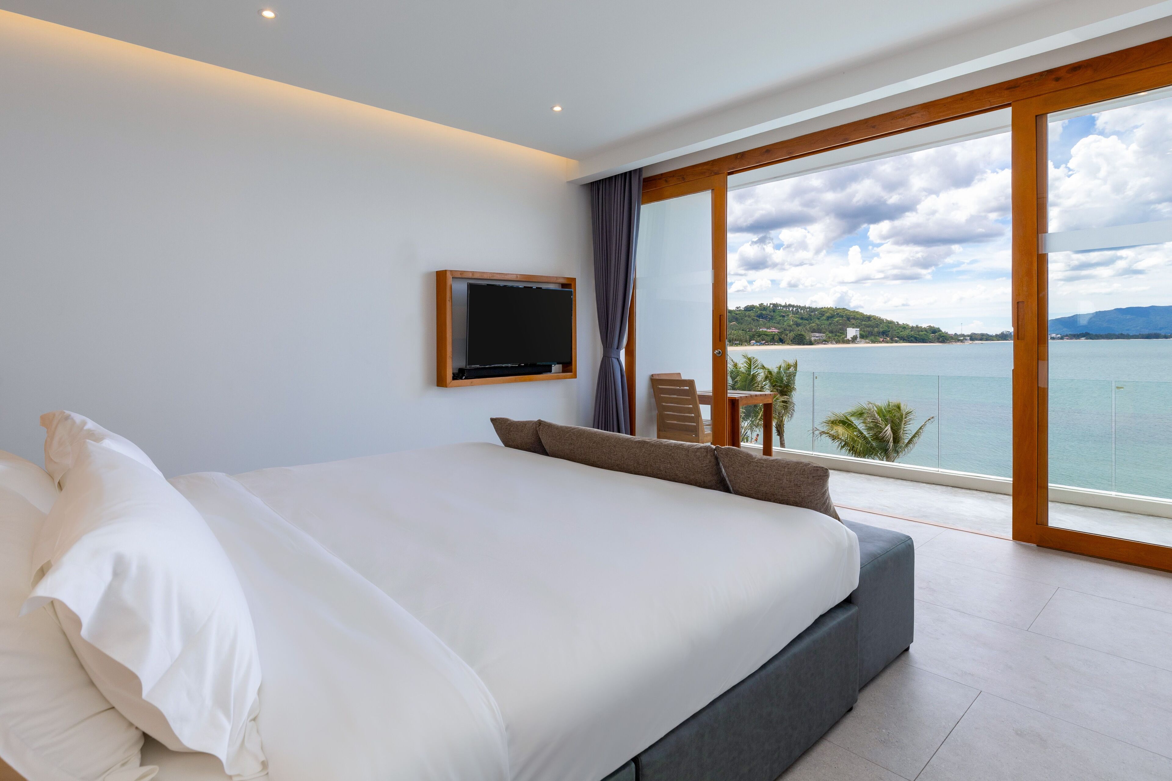 Un dormitorio con una cama grande, un televisor montado en la pared y vistas al mar a través de amplias ventanas.