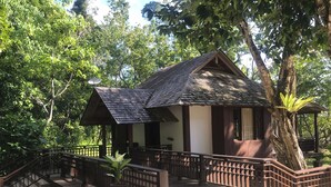 A traditional wooden house with a tiled roof, surrounded by lush greenery and a stone staircase leading to a wooden deck. - Saujana Private Villas (Langkawi)