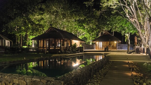 A nighttime view of a resort with two wooden cabins, a reflecting pool, and a stone pathway. - Saujana Private Villas (Langkawi)
