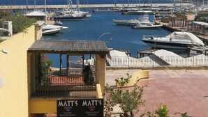 A marina with boats docked, a building with a sign for 'Matt's Cafe', and a view of the sea and hills in the background. - Elegant and spacious apartment with terrace and gulf view in Costa Smeralda  (Olbia)