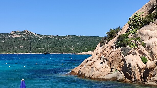 A coastal scene with clear blue water, rocky cliffs, and a sailboat in the distance. - Elegant and spacious apartment with terrace and gulf view in Costa Smeralda  (Olbia)