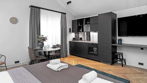 A modern hotel room with a bed, a dining table, a kitchen area, and a TV mounted on the wall. - Backyard Stylish Studio for 2 - Excellent Location (Reykjavík)