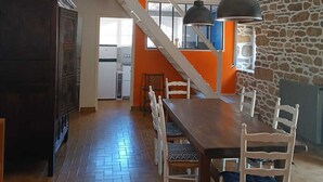 A dining area with a wooden table and chairs, a staircase, and a kitchen in the background. - Maison Dans Propriété Arborée, à 800m de la Plage (Plounéour-Brignogan-plages)