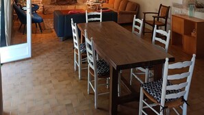 A cozy living room with a stone wall fireplace, a wooden dining table, and a comfortable seating area. - Maison Dans Propriété Arborée, à 800m de la Plage (Plounéour-Brignogan-plages)