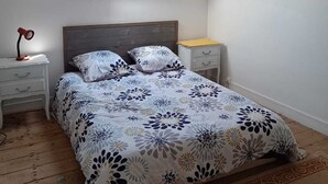 A bedroom with a sloped ceiling, a skylight, a bed with a floral bedspread, a bedside table with a lamp, and a nightstand with a lamp. - Maison Dans Propriété Arborée, à 800m de la Plage (Plounéour-Brignogan-plages)