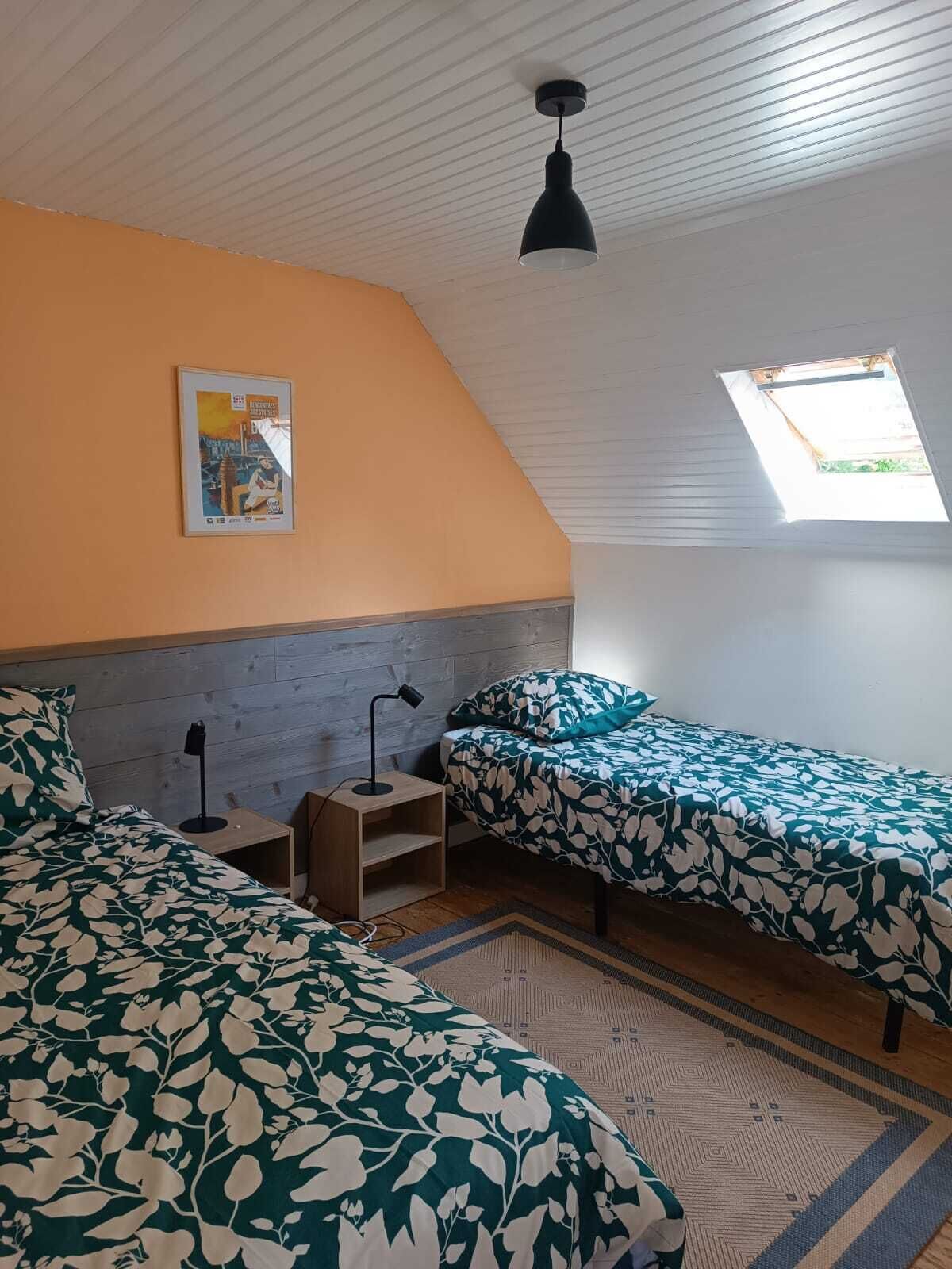 Een slaapkamer met twee bedden, een dakraam, een poster aan de muur en een klein tafeltje met een lamp.