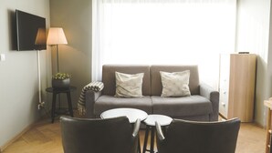 A modern living room with a grey sofa, two white cushions, a small round table, and a floor lamp. - Saga Studio for 4 guests in Downtown Gerður (Reykjavík)