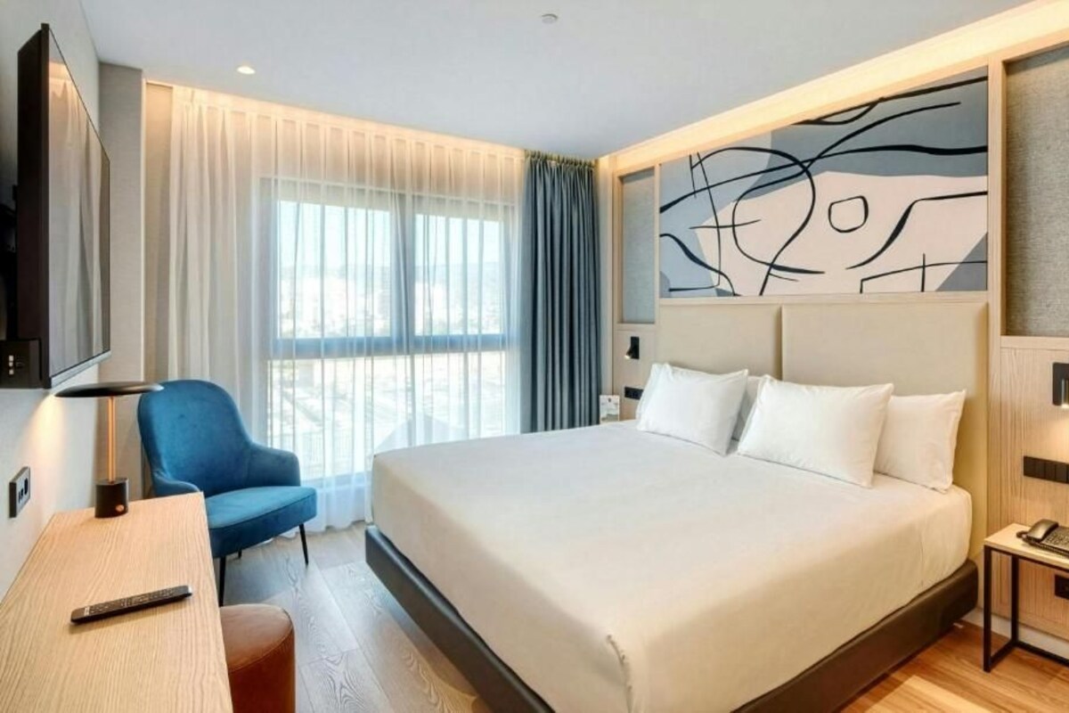 Habitación de hotel con una cama grande, un escritorio con una silla, un televisor y una ventana con cortinas.