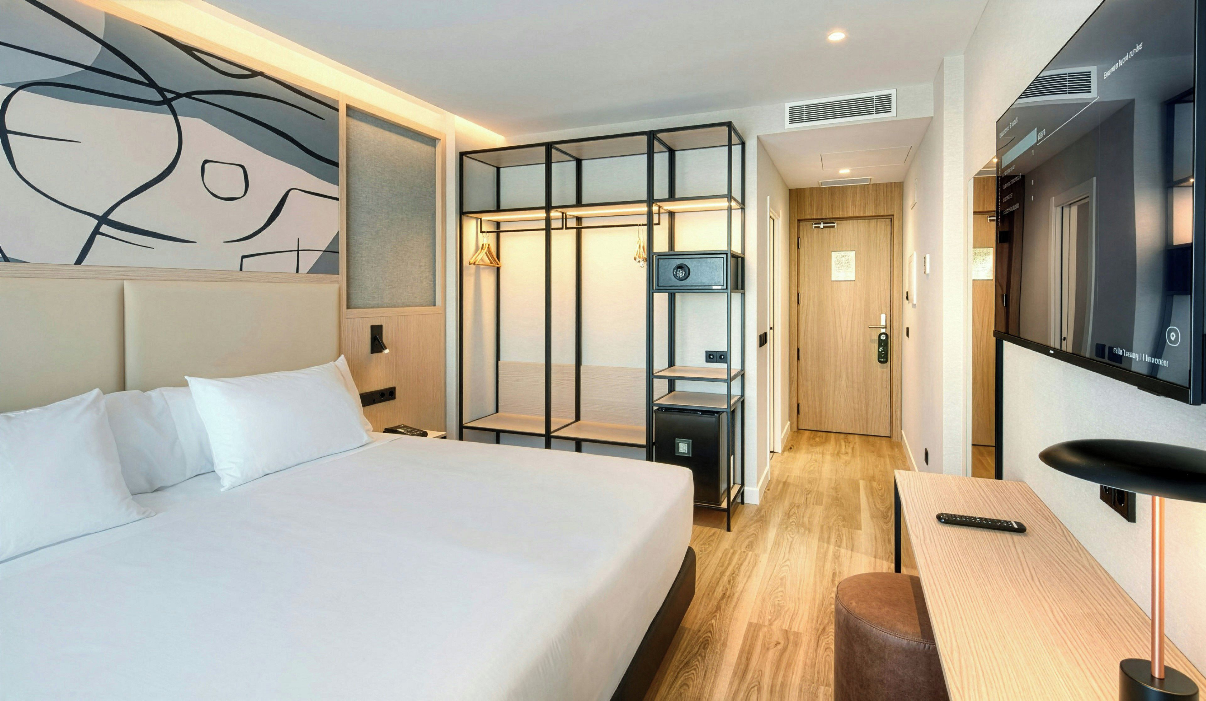 A hotel room with a large bed, a desk, a TV, and a wardrobe.