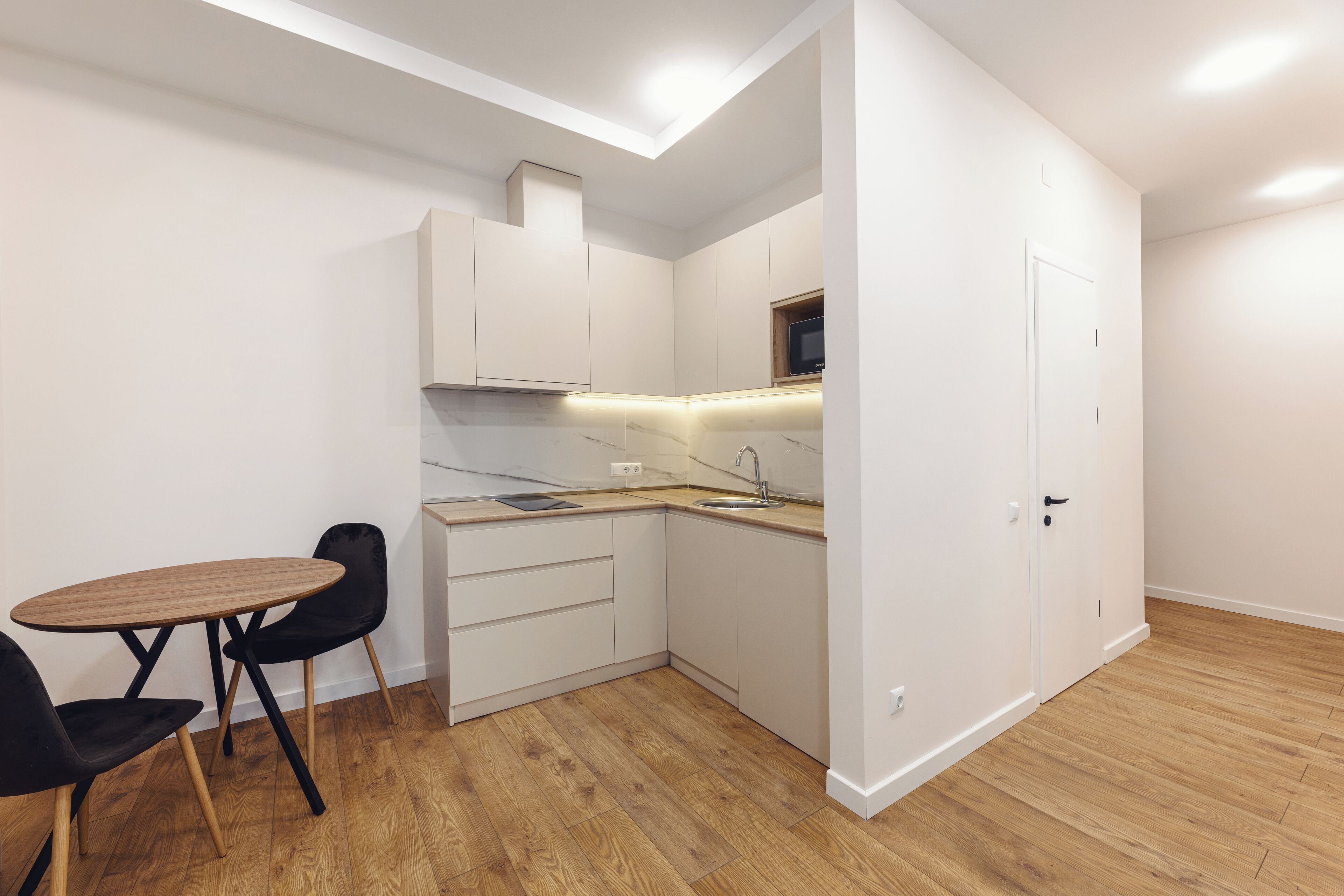 A compact kitchen with a dining area, featuring white cabinetry, a wooden countertop, and a small dining table with chairs.