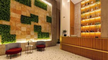 A lobby with a reception desk, two armchairs, a wall with green plants, and a tiled floor.