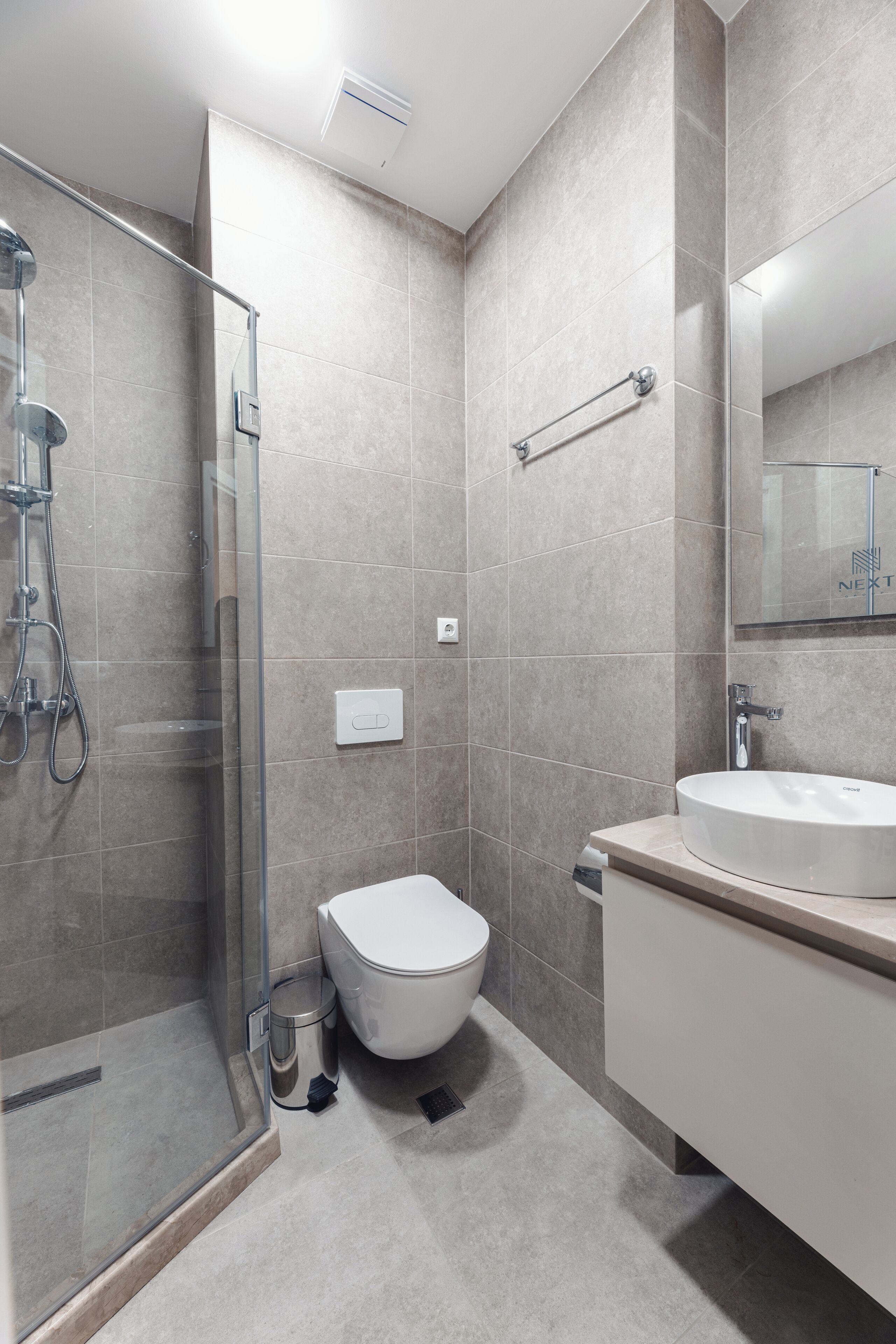 A modern bathroom with a glass-enclosed shower, a toilet, and a sink.