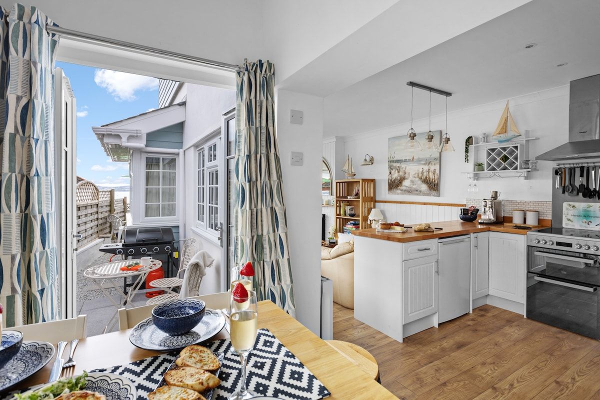 A modern kitchen with white cabinetry, a dining area with a table set for two, and a view of the outside.