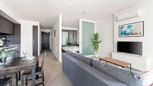 A modern apartment with a dining area, a living room with a sofa, a TV, and a kitchen.