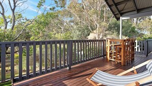 A wooden deck with a table and chairs, surrounded by a black railing, overlooking a natural landscape. - Pet-Friendly, WiFi & Pool Table | Two Salty Dogs (Lilli Pilli)