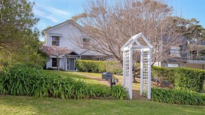A two-story house with a front yard, a mailbox, and a white trellis structure. - Pet-Friendly, WiFi & Pool Table | Two Salty Dogs (Lilli Pilli)