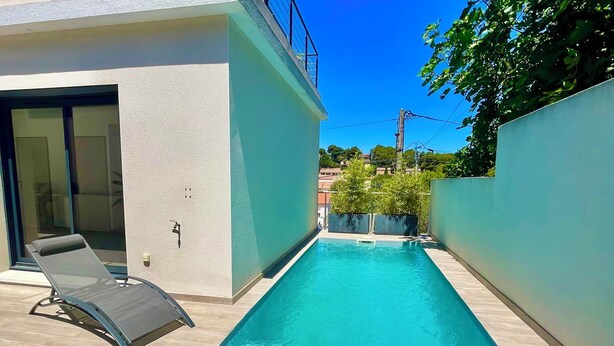 A modern outdoor pool area with a clear blue pool, a lounge chair, and a sunbed.