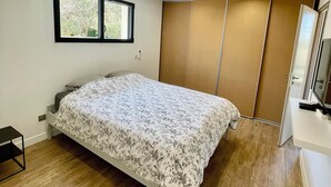 A bedroom with a bed, a window, a wardrobe, and a desk.