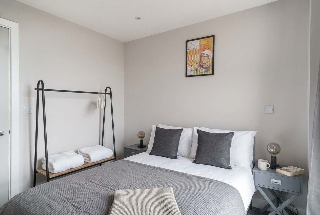 Un dormitorio con cama, mesita de noche, una obra de arte en la pared y una silla colgante.