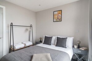 Une chambre à coucher comprenant un lit, une table de chevet, une commode, une œuvre d’art accrochée au mur et un fauteuil suspendu.