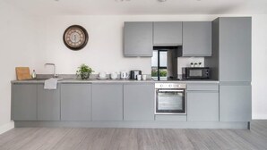 Une cuisine moderne avec des meubles gris, un four encastré, un four à micro-ondes et une horloge murale.