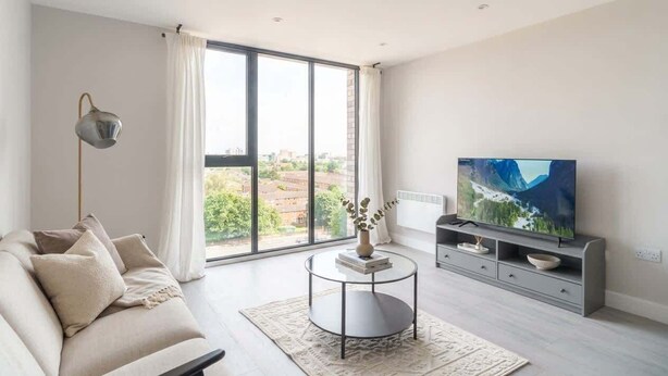 Un salon moderne avec un canapé, une table basse, un téléviseur et une grande fenêtre donnant sur un beau paysage.