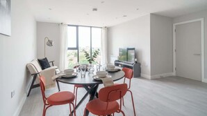Un salon moderne avec une table de salle à manger ronde, des chaises rouges, un canapé, un téléviseur et une grande fenêtre.